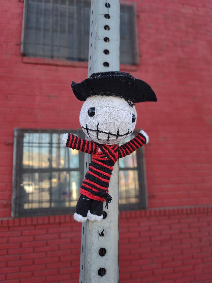 White yarn character in a black hat and red striped outfit, photographed by the artist